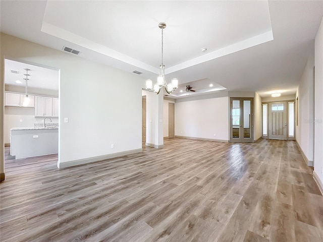 unfurnished living room featuring a raised ceiling and light hardwood / wood-style floors