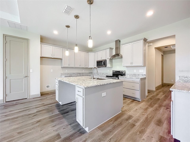 kitchen with appliances with stainless steel finishes, wall chimney exhaust hood, sink, a center island with sink, and white cabinets