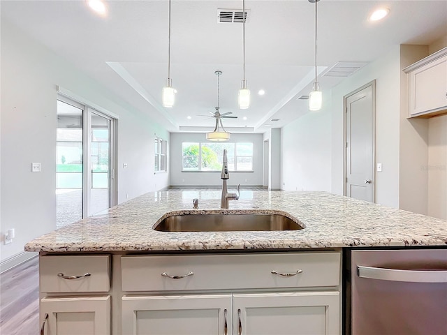 kitchen with light stone countertops, sink, hanging light fixtures, light hardwood / wood-style flooring, and a kitchen island with sink