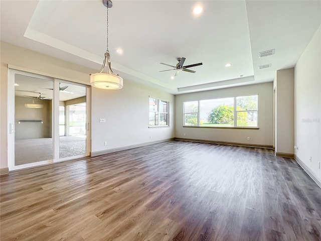 empty room with ceiling fan, dark hardwood / wood-style flooring, and a tray ceiling