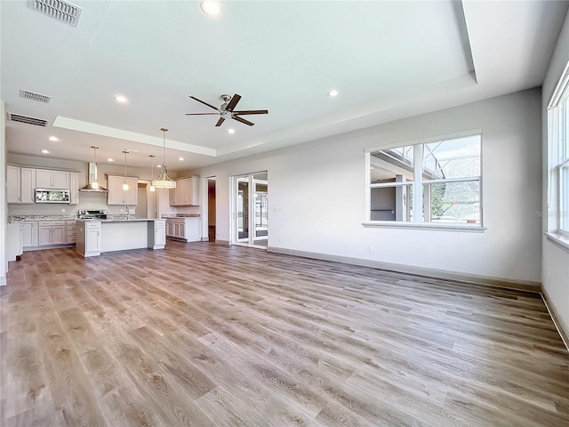 unfurnished living room with light wood-type flooring, a raised ceiling, and ceiling fan