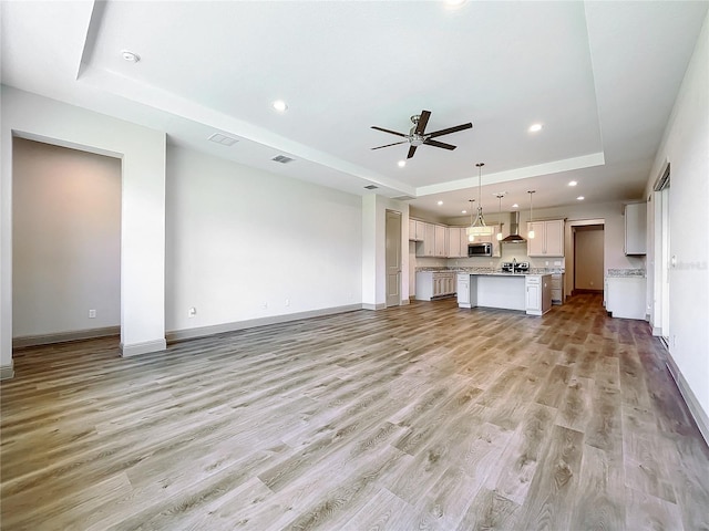 unfurnished living room with a tray ceiling, ceiling fan, and wood-type flooring