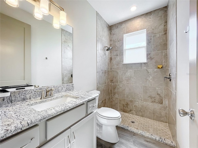 bathroom featuring hardwood / wood-style flooring, vanity, toilet, and a tile shower