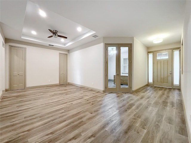 unfurnished living room featuring a raised ceiling, ceiling fan, french doors, and light hardwood / wood-style floors