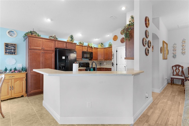 kitchen featuring backsplash, light hardwood / wood-style flooring, lofted ceiling, and black appliances