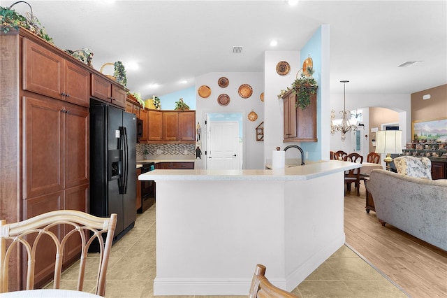 kitchen with tasteful backsplash, black refrigerator with ice dispenser, pendant lighting, a chandelier, and light hardwood / wood-style floors