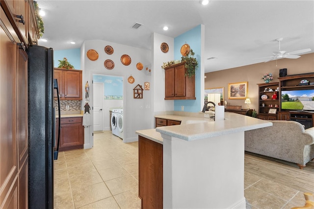 kitchen with backsplash, black fridge, sink, washing machine and dryer, and kitchen peninsula