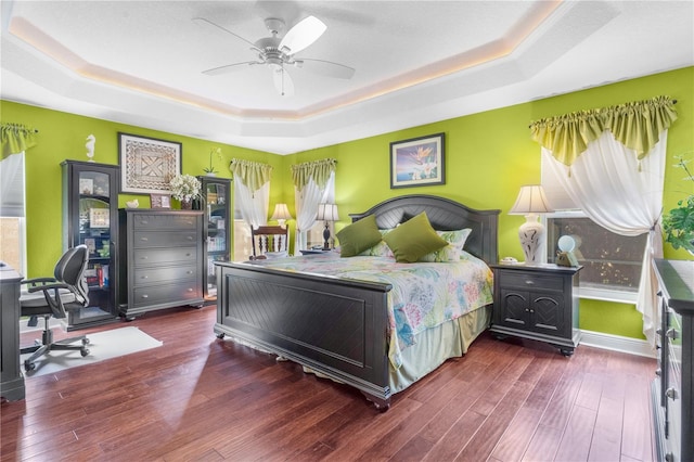 bedroom featuring a raised ceiling, ceiling fan, and dark wood-type flooring