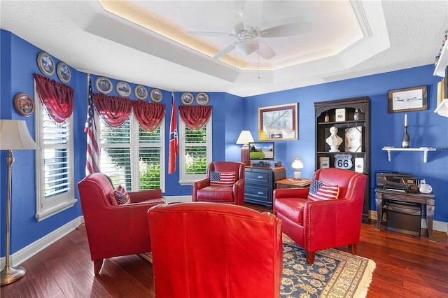 living room with ceiling fan, dark hardwood / wood-style flooring, and a tray ceiling