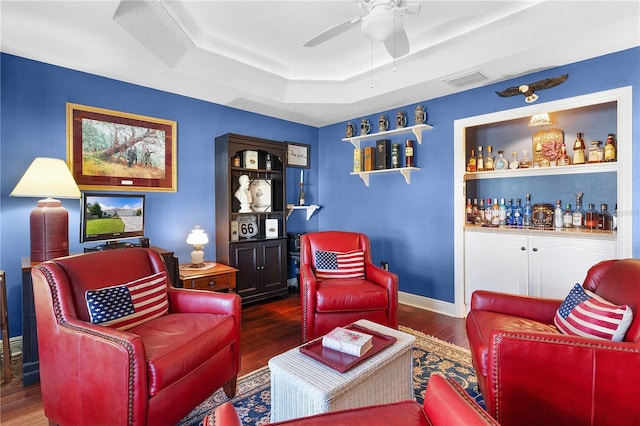 living room featuring dark hardwood / wood-style floors, a raised ceiling, bar, and ceiling fan