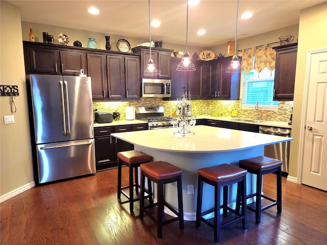 kitchen with appliances with stainless steel finishes, dark hardwood / wood-style flooring, sink, pendant lighting, and a kitchen island