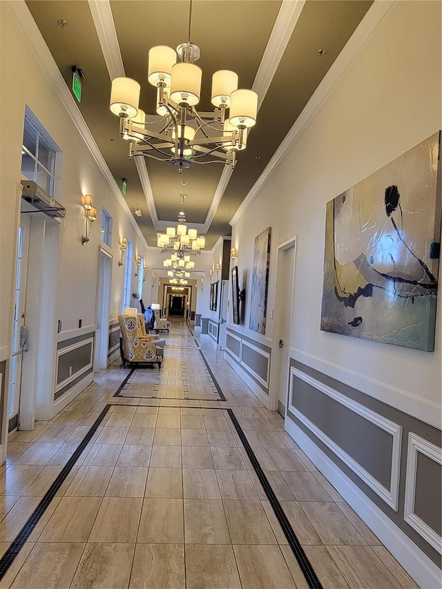 hall featuring a tray ceiling, ornamental molding, and an inviting chandelier