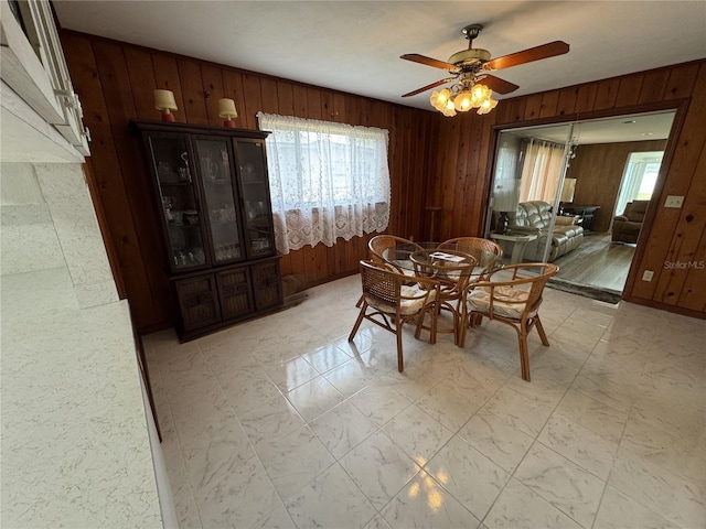 dining area with ceiling fan and wood walls