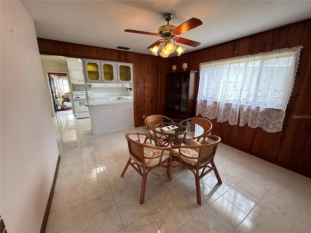 unfurnished dining area with ceiling fan and wood walls