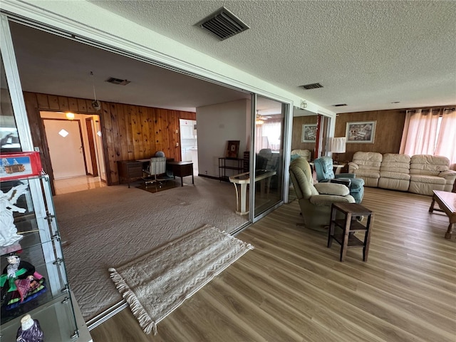 living room featuring wood-type flooring, wooden walls, and a textured ceiling