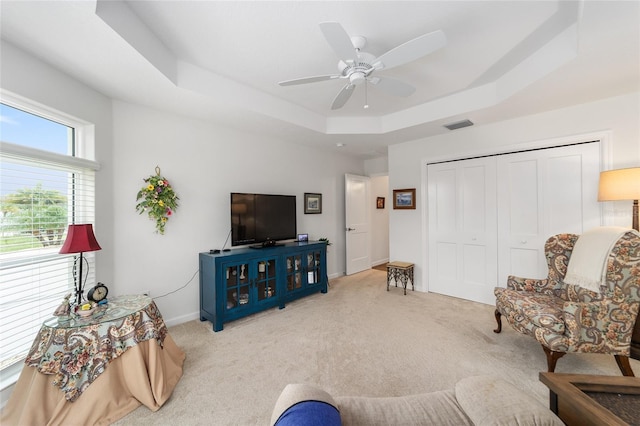 carpeted living room with a tray ceiling and ceiling fan