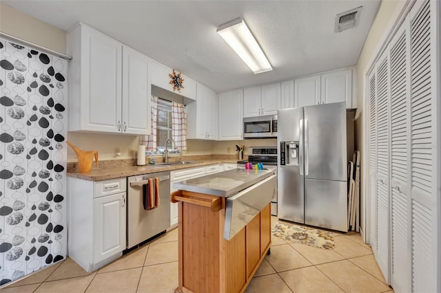 kitchen with sink, light tile patterned floors, a kitchen island, white cabinetry, and stainless steel appliances