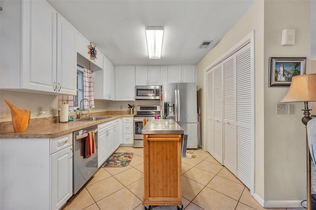 kitchen with a center island, sink, light tile patterned floors, white cabinets, and appliances with stainless steel finishes