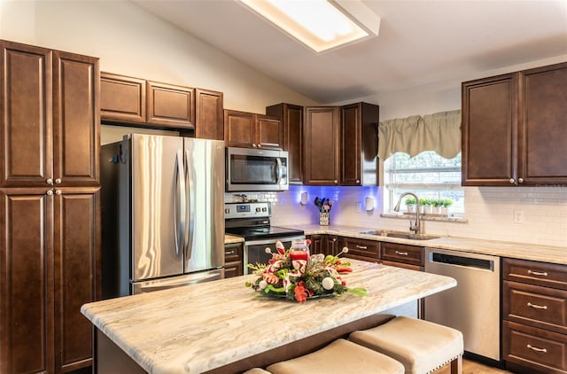 kitchen with a kitchen bar, decorative backsplash, stainless steel appliances, sink, and a kitchen island