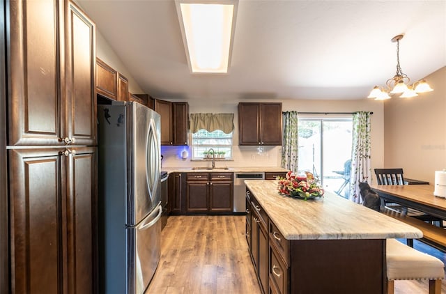 kitchen with a center island, hanging light fixtures, an inviting chandelier, appliances with stainless steel finishes, and light wood-type flooring