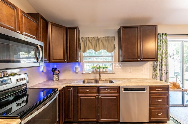 kitchen featuring dark brown cabinetry, sink, stainless steel appliances, light stone counters, and backsplash