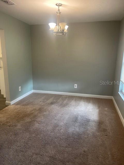 empty room featuring dark carpet and an inviting chandelier