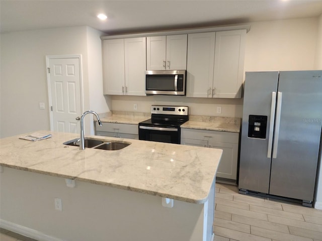 kitchen with a kitchen island with sink, sink, light hardwood / wood-style flooring, light stone countertops, and stainless steel appliances