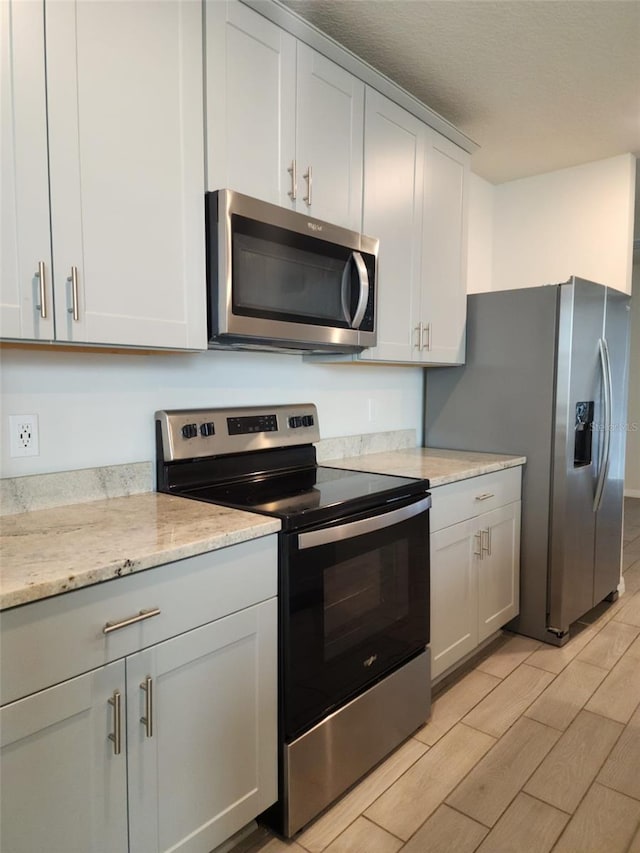 kitchen featuring light stone counters, a textured ceiling, stainless steel appliances, white cabinets, and light hardwood / wood-style floors