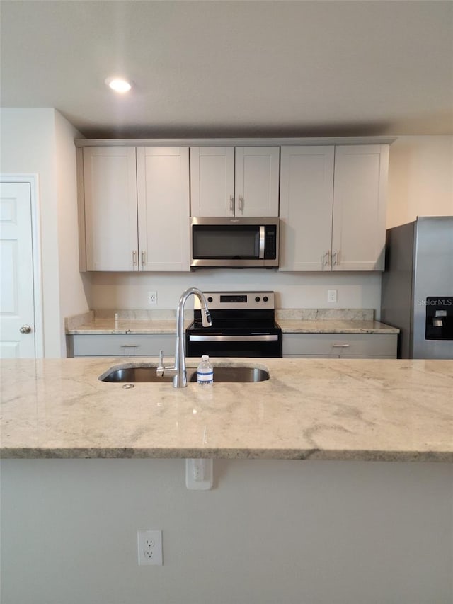 kitchen featuring light stone countertops, appliances with stainless steel finishes, white cabinets, and sink