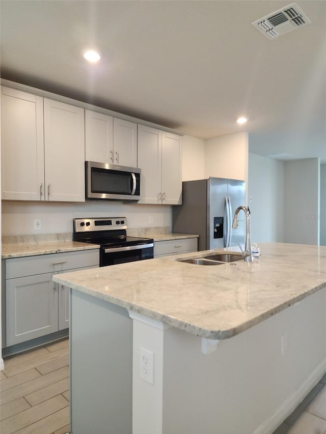 kitchen featuring light stone countertops, sink, light hardwood / wood-style flooring, an island with sink, and appliances with stainless steel finishes