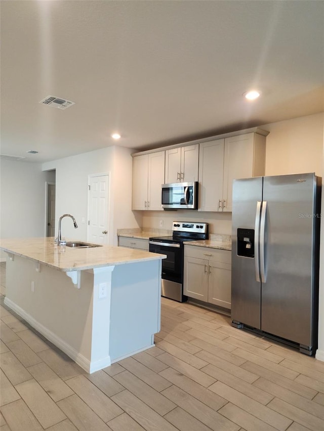 kitchen featuring appliances with stainless steel finishes, light stone counters, sink, light hardwood / wood-style floors, and an island with sink