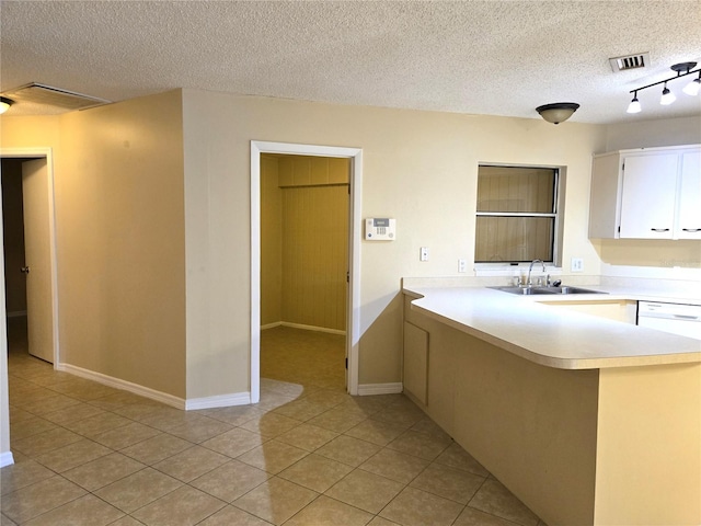 kitchen with sink, light tile patterned floors, kitchen peninsula, a textured ceiling, and white cabinets