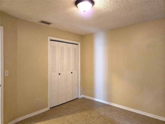 unfurnished bedroom with tile patterned floors, a textured ceiling, and a closet