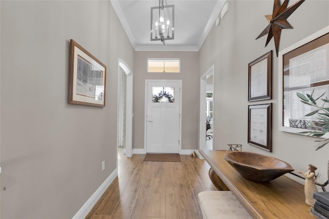 entryway featuring a towering ceiling, light hardwood / wood-style floors, crown molding, and a notable chandelier