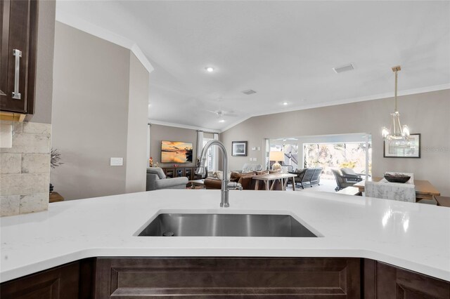 kitchen with light stone countertops, sink, lofted ceiling, decorative light fixtures, and dark brown cabinets