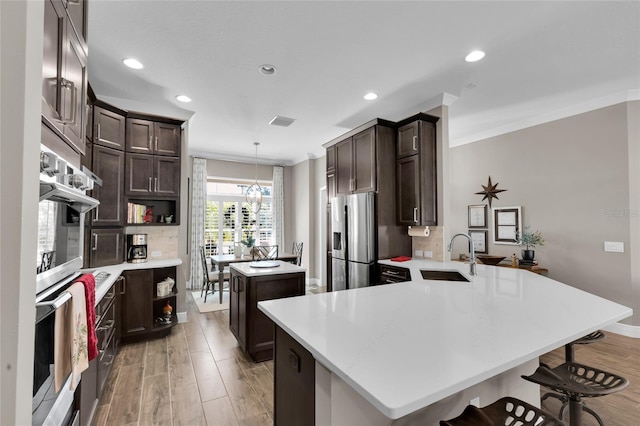 kitchen featuring sink, stainless steel fridge with ice dispenser, kitchen peninsula, pendant lighting, and a kitchen bar