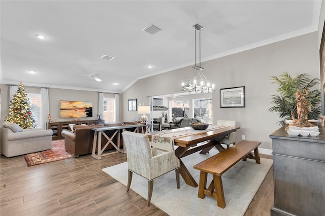 dining space with vaulted ceiling, hardwood / wood-style floors, ceiling fan with notable chandelier, and ornamental molding