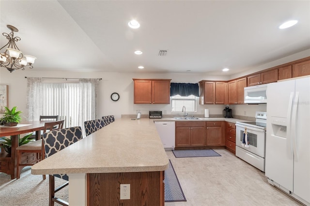 kitchen with a notable chandelier, kitchen peninsula, pendant lighting, white appliances, and a breakfast bar area