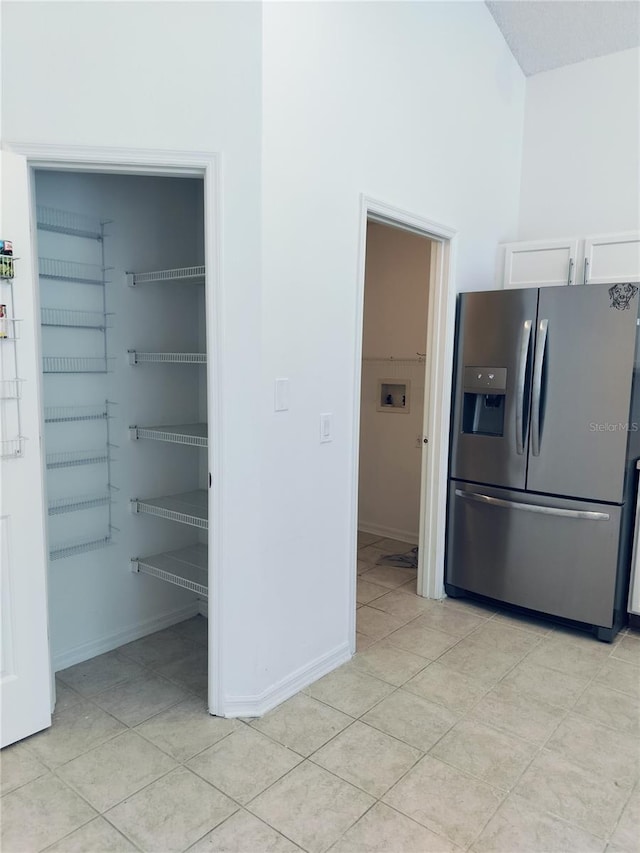 kitchen with stainless steel refrigerator with ice dispenser, white cabinetry, and light tile patterned flooring