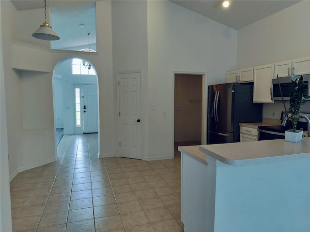 kitchen featuring white cabinets, a towering ceiling, hanging light fixtures, and appliances with stainless steel finishes