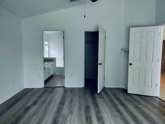 unfurnished bedroom with ensuite bathroom, a walk in closet, vaulted ceiling, light wood-type flooring, and a closet