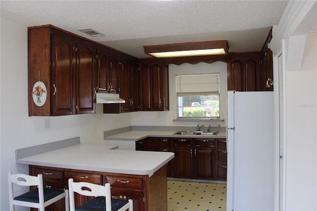 kitchen with a textured ceiling, white refrigerator, and sink