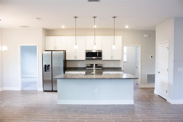 kitchen with white cabinetry, pendant lighting, dark stone counters, a kitchen island with sink, and appliances with stainless steel finishes