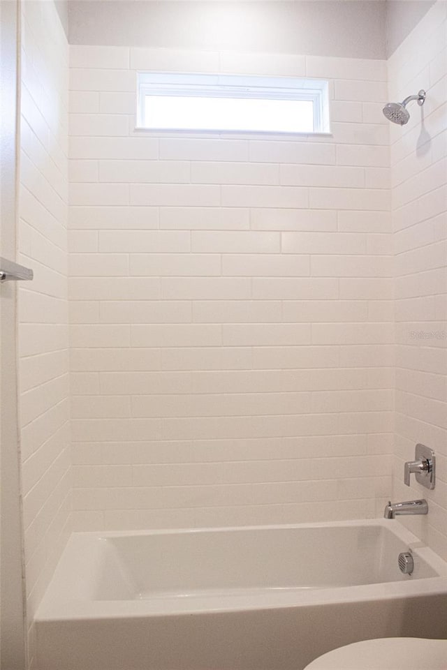 bathroom with toilet and tiled shower / bath