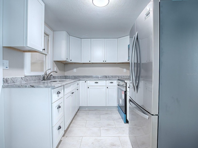 kitchen featuring light stone countertops, appliances with stainless steel finishes, a textured ceiling, sink, and white cabinetry