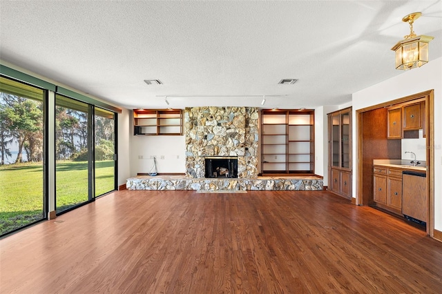 unfurnished living room featuring track lighting, dark hardwood / wood-style floors, built in features, a fireplace, and a textured ceiling