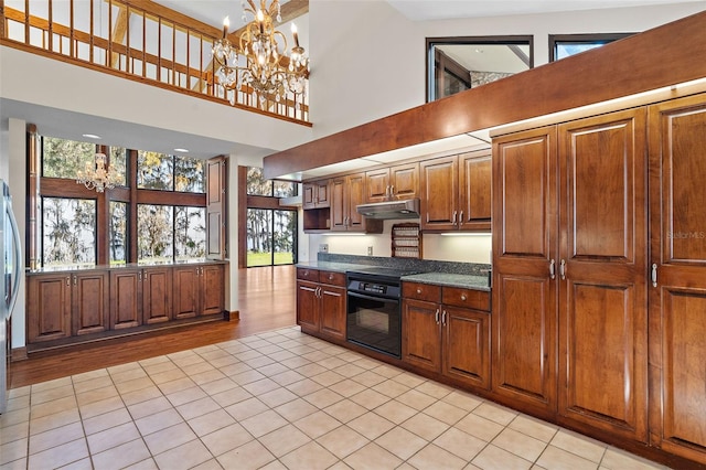 kitchen with an inviting chandelier, stainless steel fridge, a towering ceiling, black oven, and light tile patterned floors