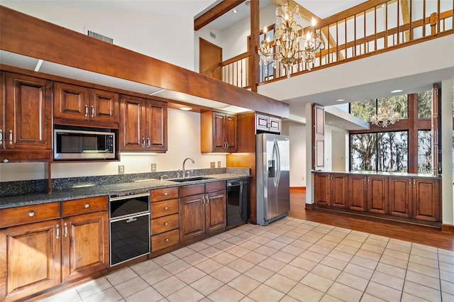 kitchen with dark stone counters, sink, light tile patterned floors, appliances with stainless steel finishes, and a notable chandelier