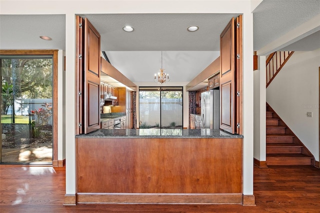 kitchen with dark stone counters, dark hardwood / wood-style floors, a textured ceiling, appliances with stainless steel finishes, and decorative light fixtures