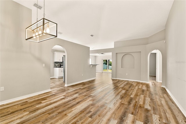 unfurnished living room with ceiling fan with notable chandelier and light hardwood / wood-style floors